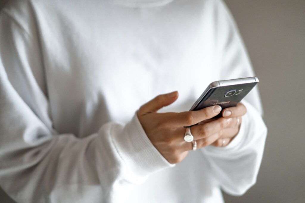 Replace impulse purchases with a budget that treats repayments as essential spending: a person in a white jumper checking their household budget on a mobile phone
